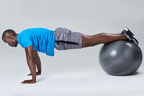 Fit healthy man uses pilates gym ball as part of toning and muscle building training exercises
