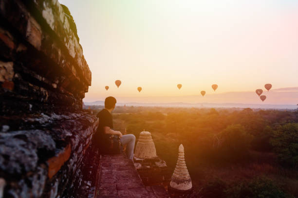 силуэт молодого мужчины пеший турист сидит и смотрит горячий воздушный шар путешествия назначения в баган, мьянма. - architecture asia morning bagan стоковые фото и изображения