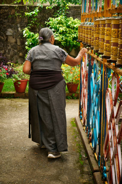 Tibetan senior woman touching prayer wheels begging for good health Pokhara, Nepal - August 20, 2017: Tibetan senior woman walking along buddhistic prayer wheels touching and turning them to beg for good health as part of their religion and spiritual culture. The woman is wearing traditional clothing typical for the Tibetan refugees living in the Tibetan refugee camp near Pokhara. XXXL (Sony Alpha 7R) prayer wheel nepal kathmandu buddhism stock pictures, royalty-free photos & images