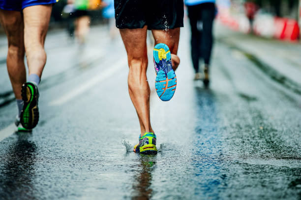 wasser spritzt unter laufschuhe läufer männer - marathon stock-fotos und bilder