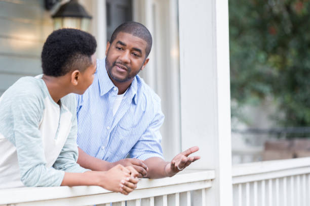 Father and son in serious front porch conversation A father talks with his hands as he leans against the railing of his front porch with his preteen son and has a serious discussion. guru photos stock pictures, royalty-free photos & images
