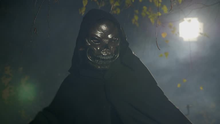 Spooky dark zombie wearing a mask playing with his black cape attacking the camera in the halloween moonlight