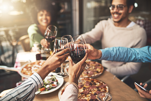 Shot of a group of cheerful young friends having a celebratory toast with wine at dinner inside of a restaurant