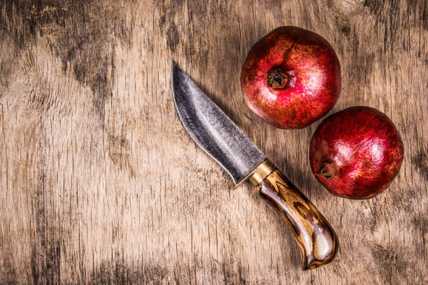 Two ripe pomegranates and knife on  wooden board. Hand knife and pomegranate. Top view. Copy space stock photo