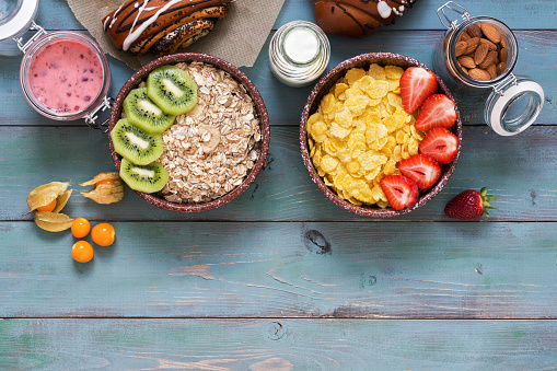 Corn flakes with strawberries and muesli with kiwi on a green wooden background. Cereals,, milk, nuts, berry mousse, fresh pastry, physalis. Healthy eating. From above, copy space