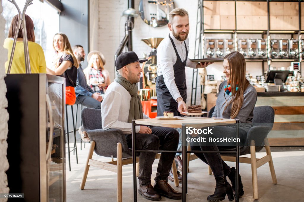 Couple ordering in the cafe Waiter bringing a sweet dessert to a young couple sitting together in the cafe Restaurant Stock Photo