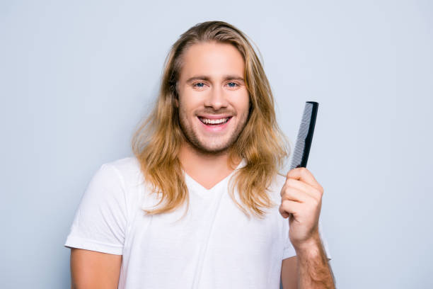 istock Concept of finding treatment against dandruff using correct shampoo and conditioner for men, close up portrait of happy joyful young guy demonstrating a comb in his hand, dressed in casual clothes 927920260