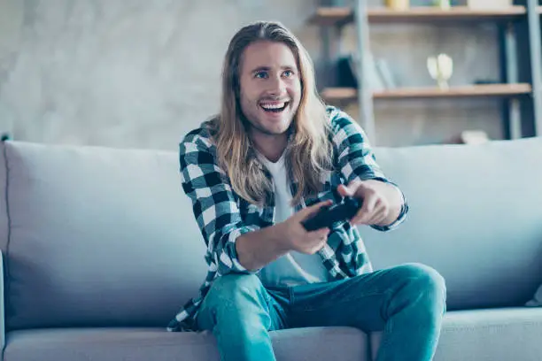 Photo of It is a perfect weekend for every man! Happy young guy is holding gamepad and playing his favourite game