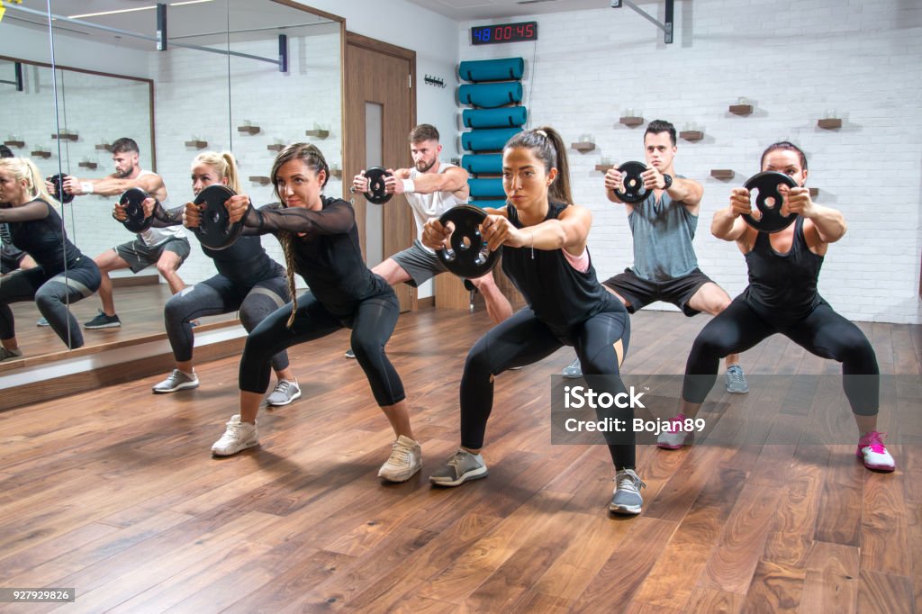 Group of sporty women and men exercising together with weight plates in health club. Group Of People Stock Photo