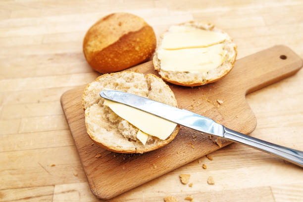 bread roll or bun with butter and knife on a cutting board on a rustic wooden table
