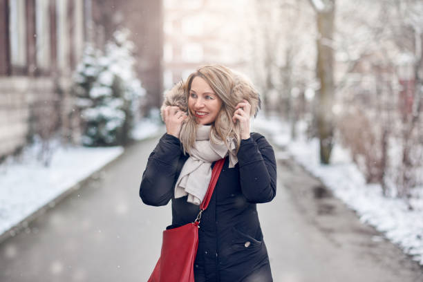Smiling young woman walking along a snowy road Smiling young woman walking along a snowy road in winter holding the fur trim on her jacket looking to the side with a happy smile one mature woman only stock pictures, royalty-free photos & images