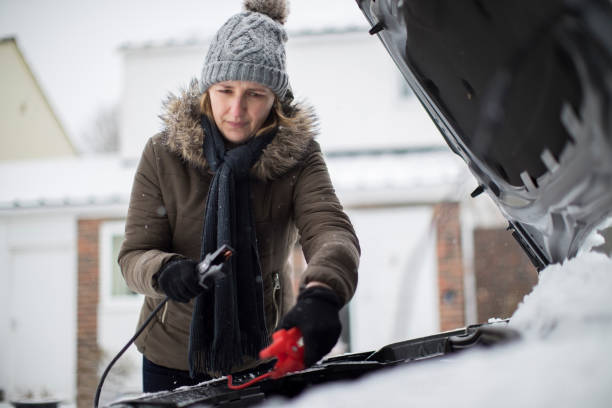 Woman Using Jumper Cables On Car Battery On Snowy Day Woman Using Jumper Cables On Car Battery On Snowy Day jumper cable stock pictures, royalty-free photos & images