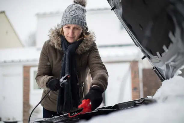 Photo of Woman Using Jumper Cables On Car Battery On Snowy Day
