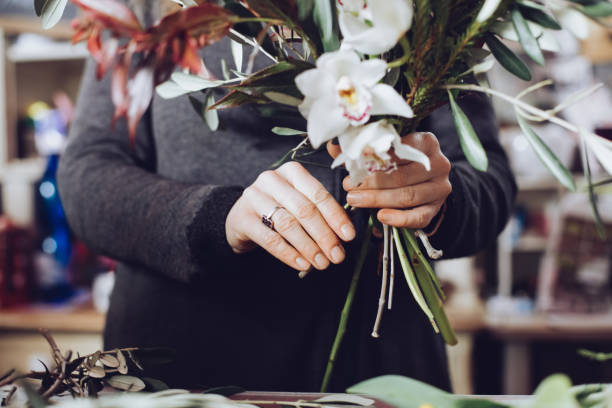 Modern florist working with flowers in workshop - with detail on hands stock photo