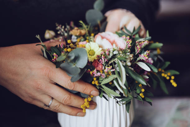Modern florist working with flowers in workshop - with detail on hands Florist handling flowers in workshop, arranging, creating bouquets, cutting, etc.. flower girl stock pictures, royalty-free photos & images