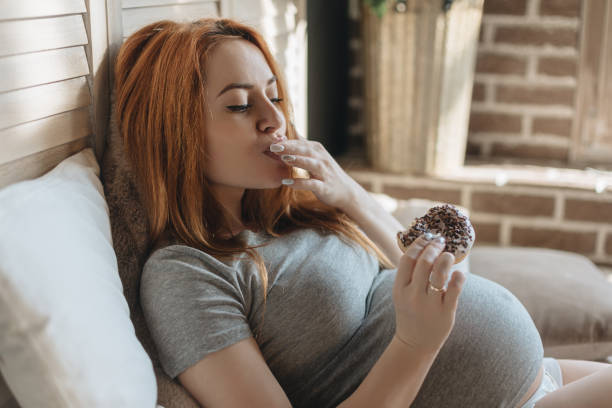 Pregnant woman eating tasty donuts stock photo