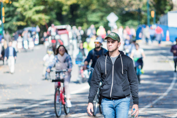 One young serious, thinking man in Midtown Manhattan with people walking on Central Park road in traffic, running, bicycles, bikes on sunny day NYC stock photo