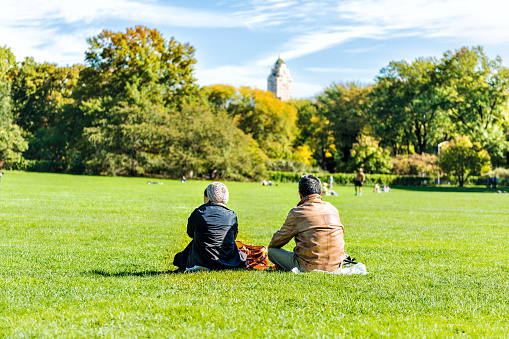 New York City, USA - October 28, 2017: Manhattan NYC Central park with couple people sitting having picnic in front of buildings skyscrapers view on great lawn grass meadow in autumn fall season