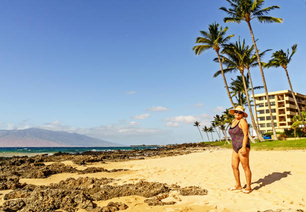 Senior Hispanic woman in bathing suit and sunhat on deserted Maui beach