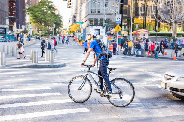 New York City, USA - October 28, 2017: Midtown Manhattan with people riding bicycles walking by Christopher Columbus Circle on sunny day, panning traffic, one young man guy
