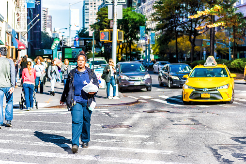 New York City, USA - October 28, 2017: Midtown Manhattan with one african american woman employee worker in blue crossing street Columbus Circle, Broadway road in traffic, carrying food lunch