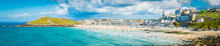 Warm afternoon light illuminating the surfers and holiday makers enjoying Porthmeor beach overlooked by the waterfront homes of St. Ives, the popular seaside resort in Cornwall, UK.