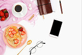 Beautiful flatlay arrangement with cup of coffee, hot waffles with cream, smartphone with black copyspace and other business accessories: concept of busy morning breakfast, white background.