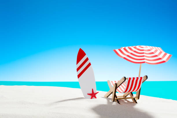 istock Deck chair under an umbrella with a surfboard on sandy beach by the sea and sky with copy space 928016254