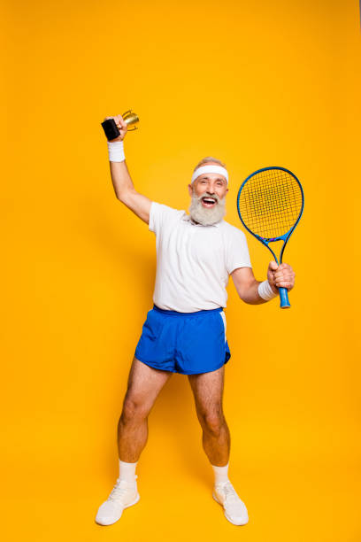 wow! competetive najlepiej cool zdrowe nowoczesne sukces aktywnego dziadka z dużym sprzętem tenisowym i nagrodę podniesioną w ręku. opieka zdrowotna, utrata masy ciała, pielęgnacja ciała, motywacja, duma, hobby - tennis men vitality joy zdjęcia i obrazy z banku zdjęć