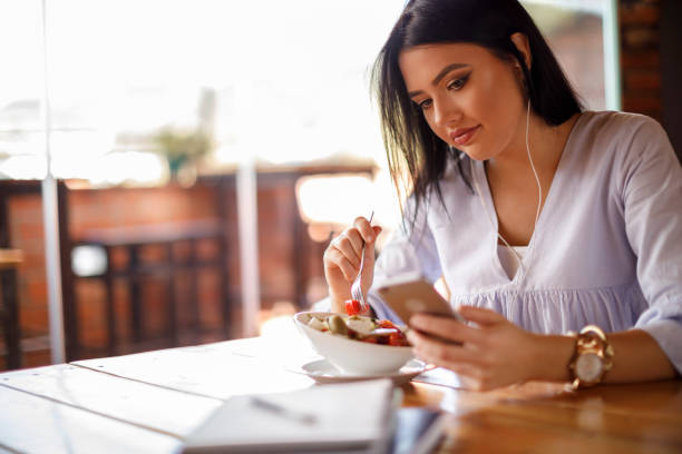 istock Female student eating salad and using mobile phone 928025140