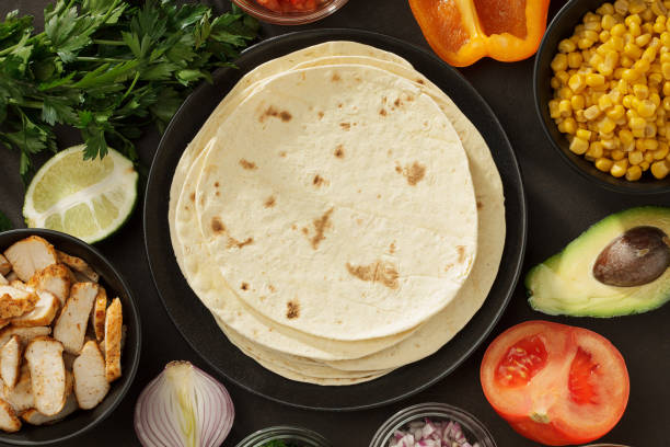 Tacos ingredients background with flatbread, fresh vegetables and roasted chicken meat on the table. stock photo