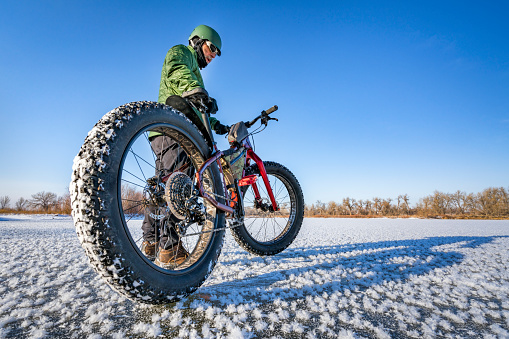 a male cyclist with his fat mountain bike on a frozen lake in northern Colorado, wide angle lens perspective