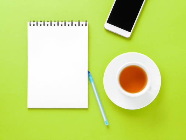 istock Top view of modern bright green office desktop with blank notepad, cup of tea, smartphone. Mock up, empty space 928047722