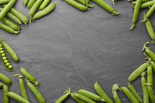 Fresh green peas pods frame on stone background, top view