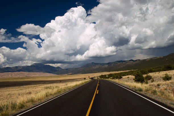 istock Paved Road and Clouds into Great Sand Dunes, Colorado 928059170