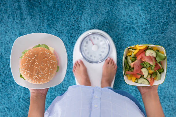 osoba trzymająca talerze burgera i sałatki - weight scale dieting weight healthcare and medicine zdjęcia i obrazy z banku zdjęć