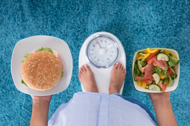 person holding plates of burger and salad - weight scale dieting weight loss imagens e fotografias de stock