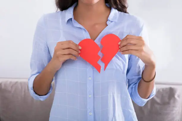 Young Woman Holding Broken Red Valentine Paper Heart At Home