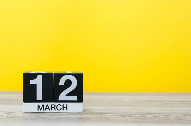 istock March 12th. Day 12 of month, calendar on table with yellow background. Spring day, empty space for text 928076696