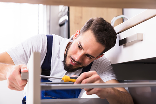 Close-up Of A Young Male Carpenter Installing Drawer With Screwdriver