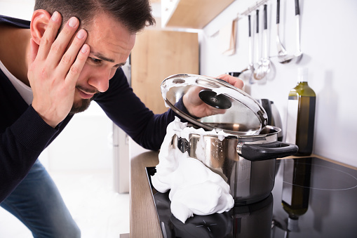 Sad Young Man Looking At Spilling Out Boiled Milk From Utensil On Induction Stove
