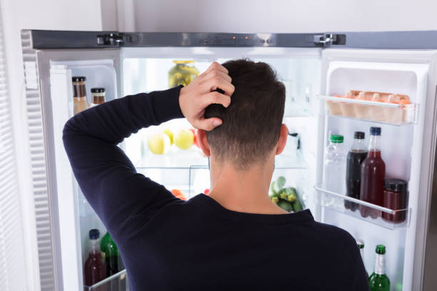 Confused Man Looking At Food In Refrigerator Rear View Of A Confused Young Man Looking At Food In Refrigerator fridge power stock pictures, royalty-free photos & images