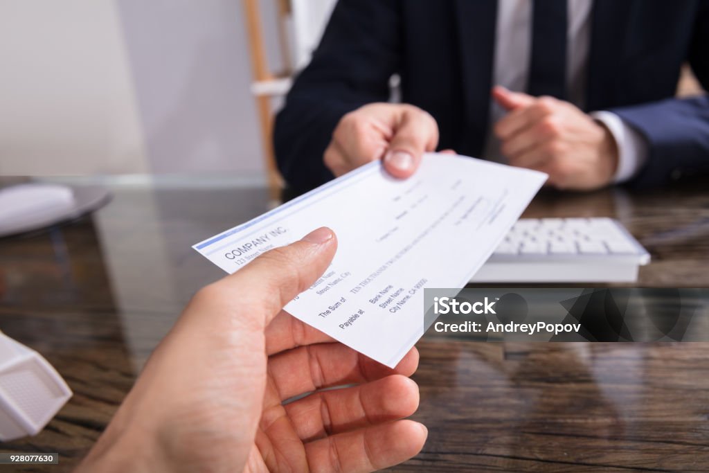 Businessperson Giving Cheque To Colleague Close-up Of A Businessperson's Hand Giving Cheque To Colleague At Workplace Check - Financial Item Stock Photo