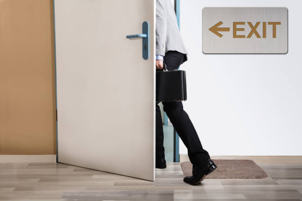 Businessperson Walking Out Businessperson Walking Out With Exit Sign On Wall quitting a job stock pictures, royalty-free photos & images
