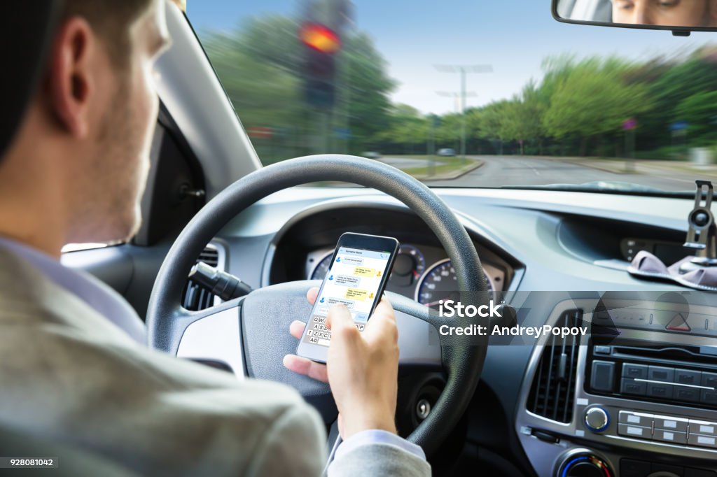 Persona que envía el mensaje de texto por teléfono móvil mientras se conduce el coche - Foto de stock de Conducir libre de derechos