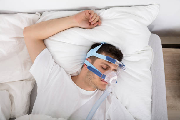 istock Man Lying On Bed With Sleeping Apnea And CPAP Machine 928084322