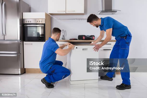 Two Movers Placing Dishwasher In Kitchen Stock Photo - Download Image Now - Installing, Appliance, Kitchen