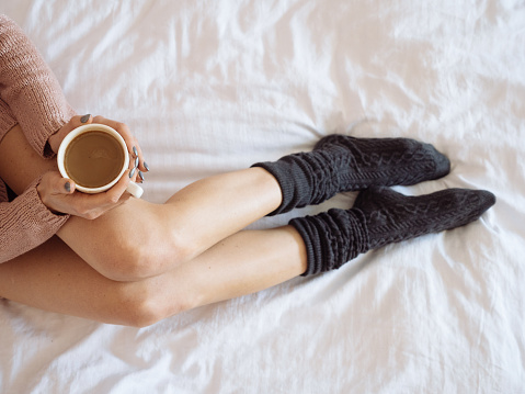 Portrait of woman on the bed with phone and cup of coffee in hands. Top view. Cozy morning.