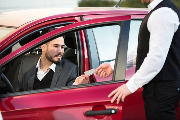 valet giving receipt to businessperson sitting inside car - valet parking imagens e fotografias de stock