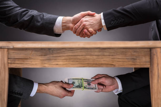 Businesspeople Shaking Hands And Taking Bribe Under Table Close-up Of Two Businesspeople Shaking Hand And Taking Bribe Under Wooden Table On Grey Background corruption stock pictures, royalty-free photos & images